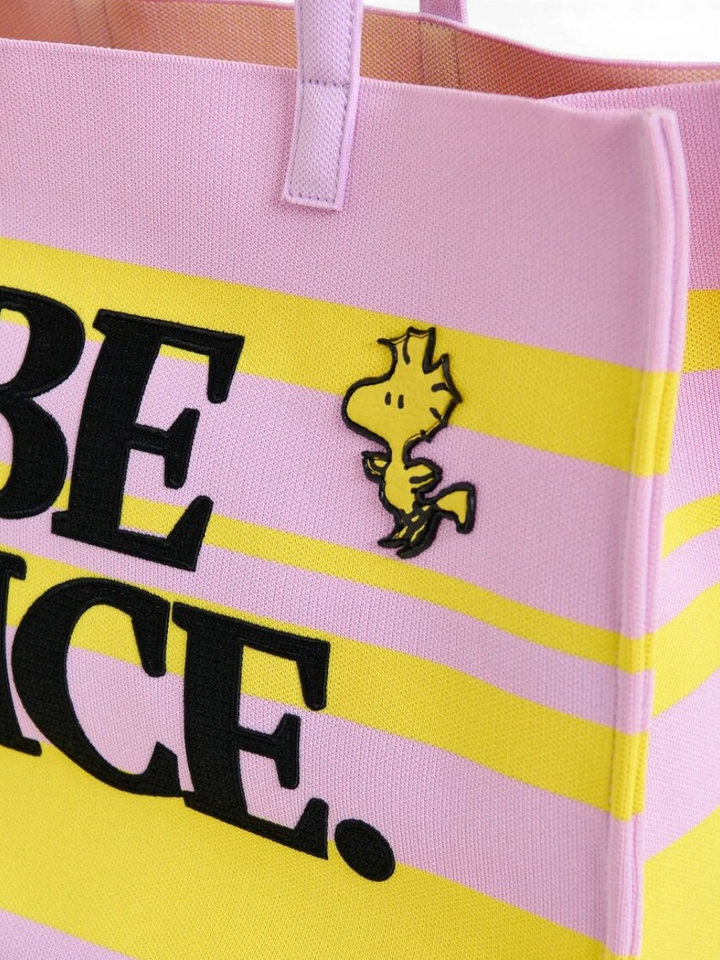 Lila en geel gestreepte boodschappentas met afbeeldingen van Peanuts Snoopy en zwarte tekst Jobba Essentiel
