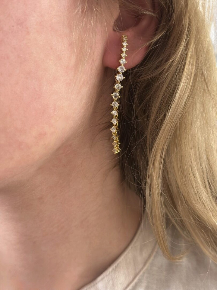 Gouden lange oorstekers met strass op het oor Ellen Beekmans